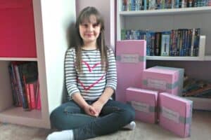 A young girl sitting in front of a book shelf