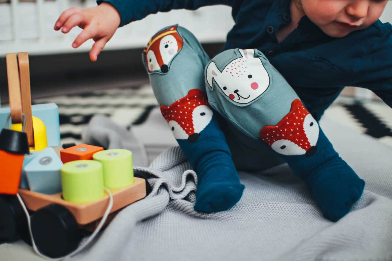 toddler wearing trousers with animal faces playing with wooden toy