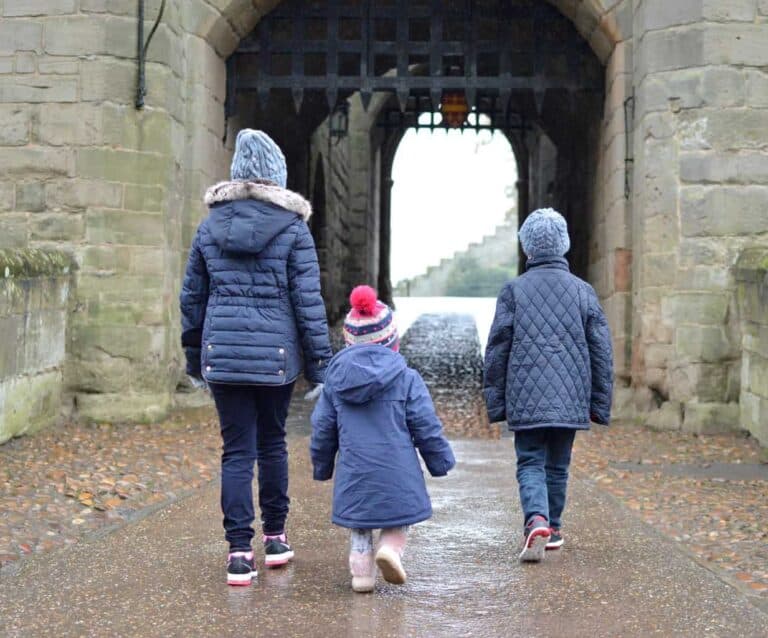 A person standing in front of a brick building, with Warwick Castle