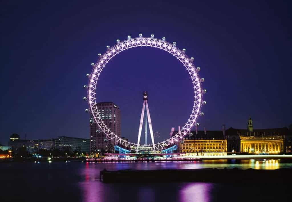 A large bridge lit up at night with London Eye in the background