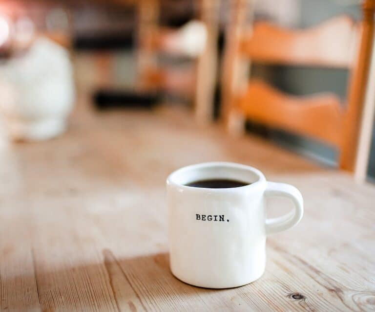 A close up of a coffee cup sitting on top of a wooden table, with Mug and Coffee bean