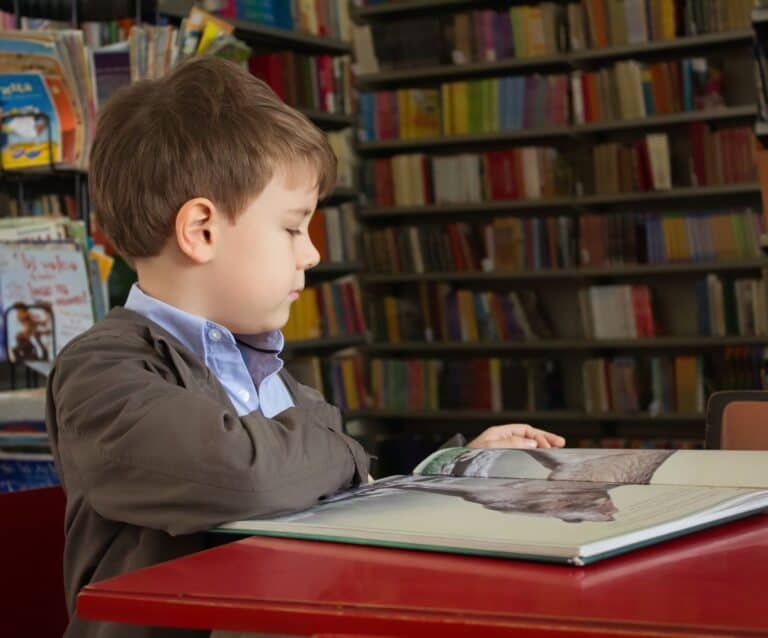 A young boy using a laptop computer sitting on top of a book shelf