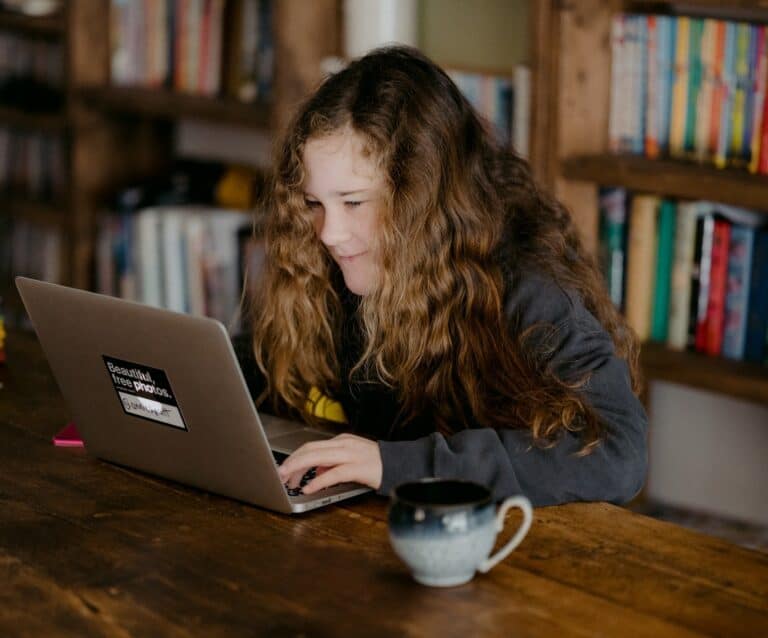 A man using a laptop computer sitting on top of a book shelf