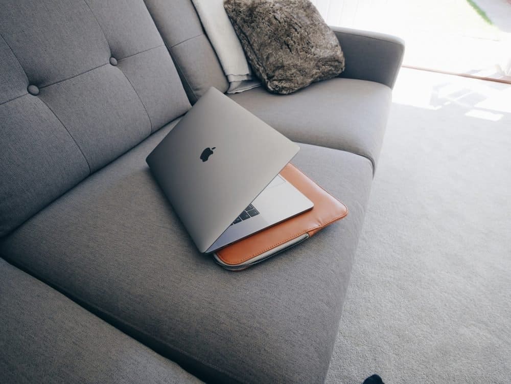 A MacBook half-open sitting on a sofa