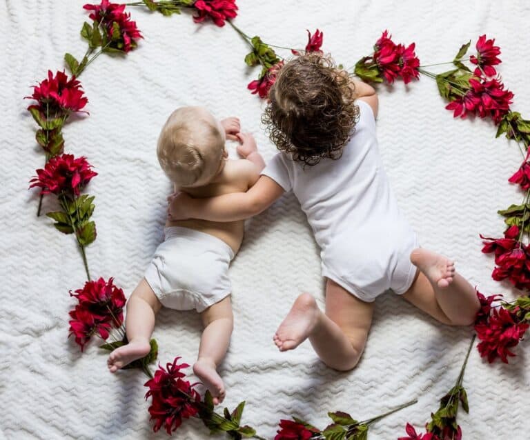 baby and toddler laying on a white blanket surrounded by flowers