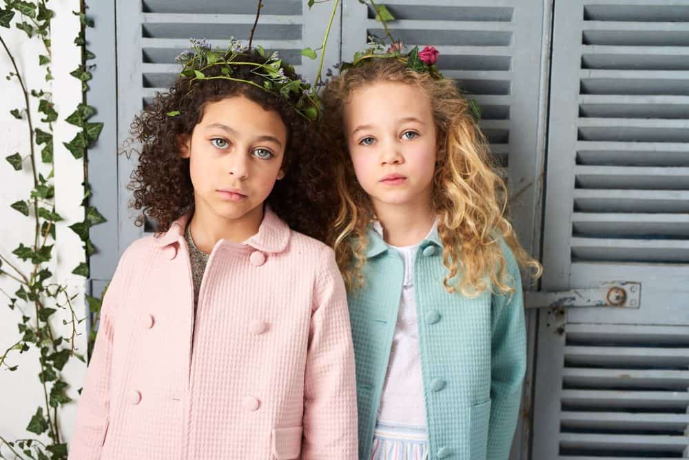 two children standing against shutters wearing coats