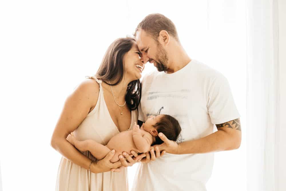 post-pregnancy - man in white crew-neck t-shirt kissing a woman in a white dress holding a newborn