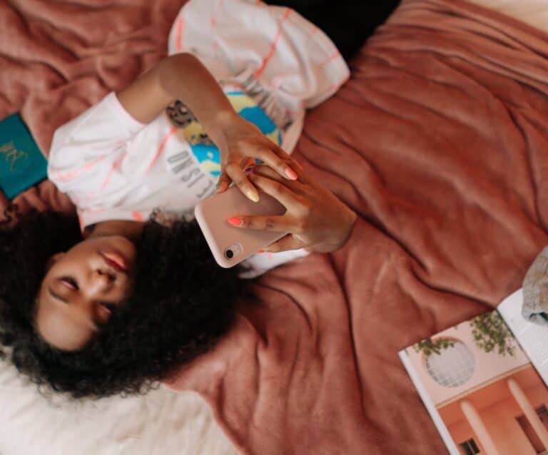 Entertaining Your Older Children - young girl lying on bed holding a cellphone