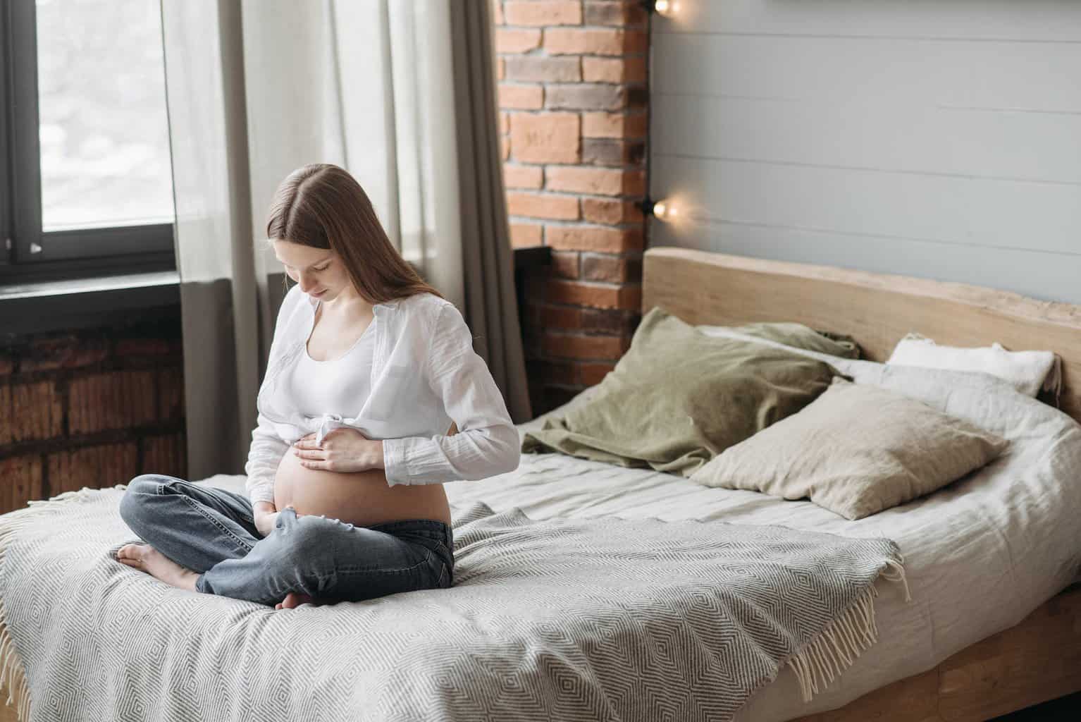 mortgage on maternity leave - pregnant woman sitting on bed holding her belly