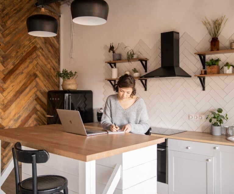 busy female freelancer with laptop taking notes in kitchen