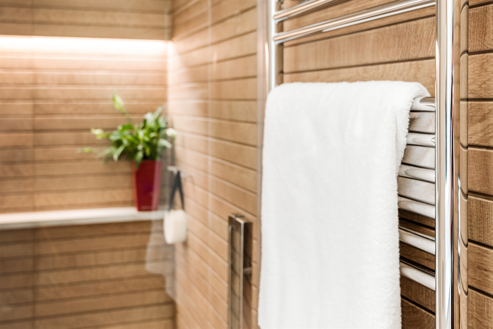 Wooden bathroom interior with heated towel rail and white towel on it. Space-Saving Solutions with Radiators
