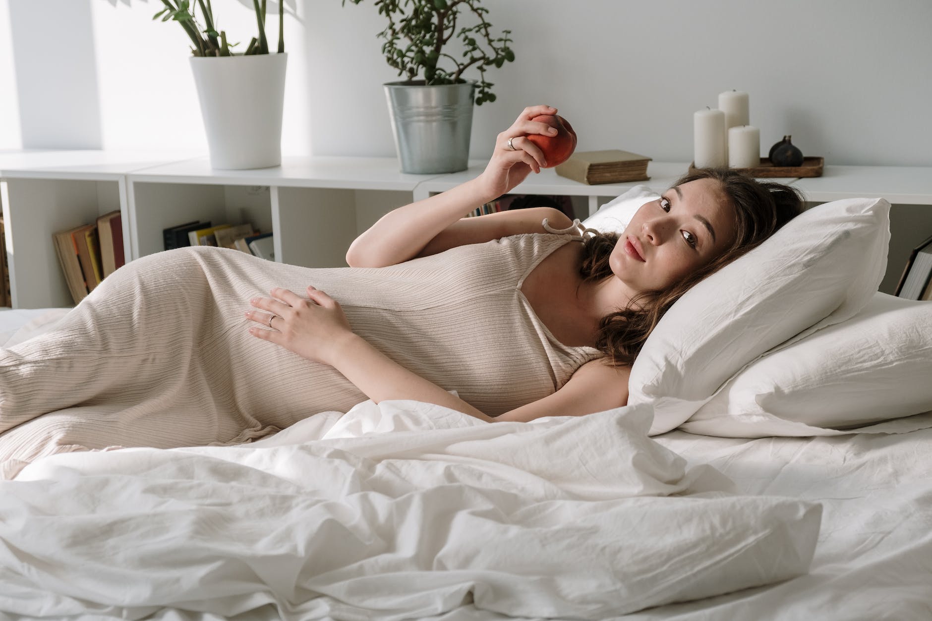 pregnant woman lying on bed with pillows holding apple
