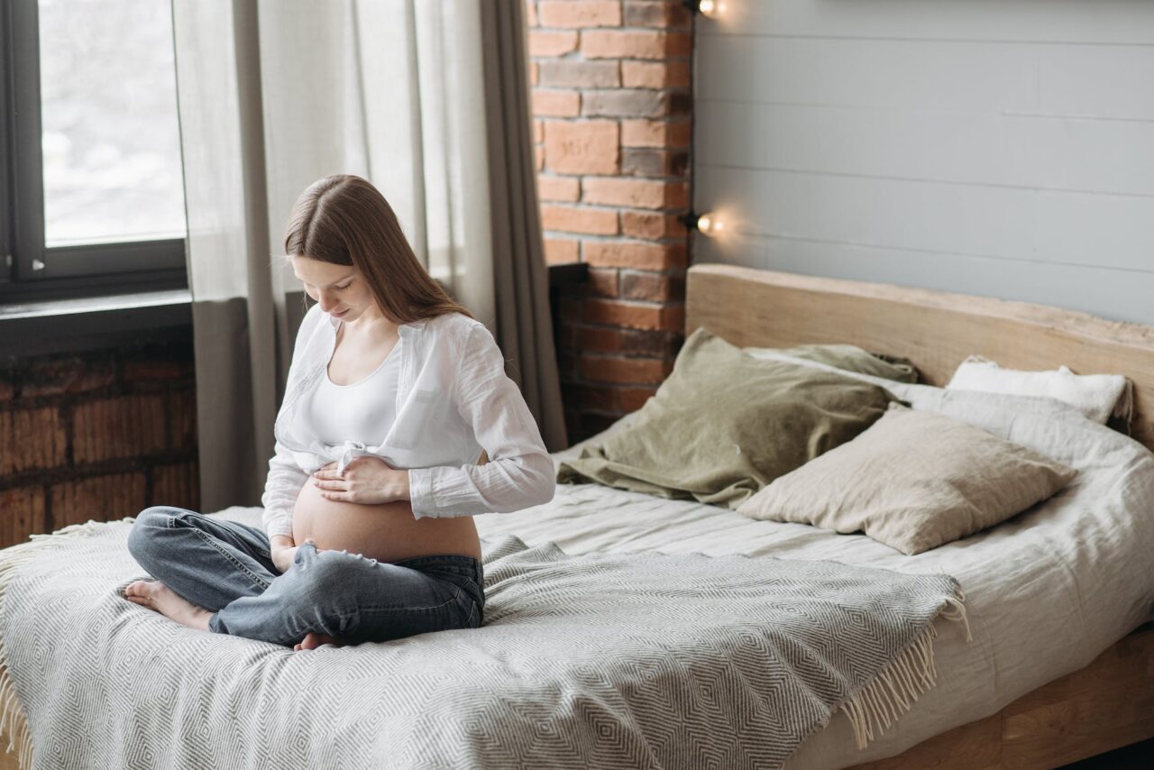 8 ways to sleep better when you're 8 months pregnant - pregnant woman sitting on bed holding her belly